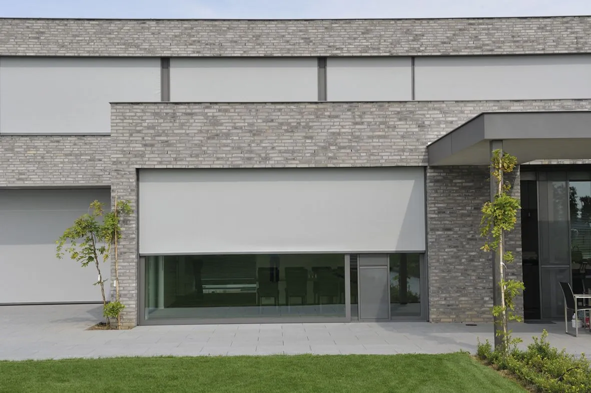 Store screen déployé devant la baie vitrée d’une maison en briques grises