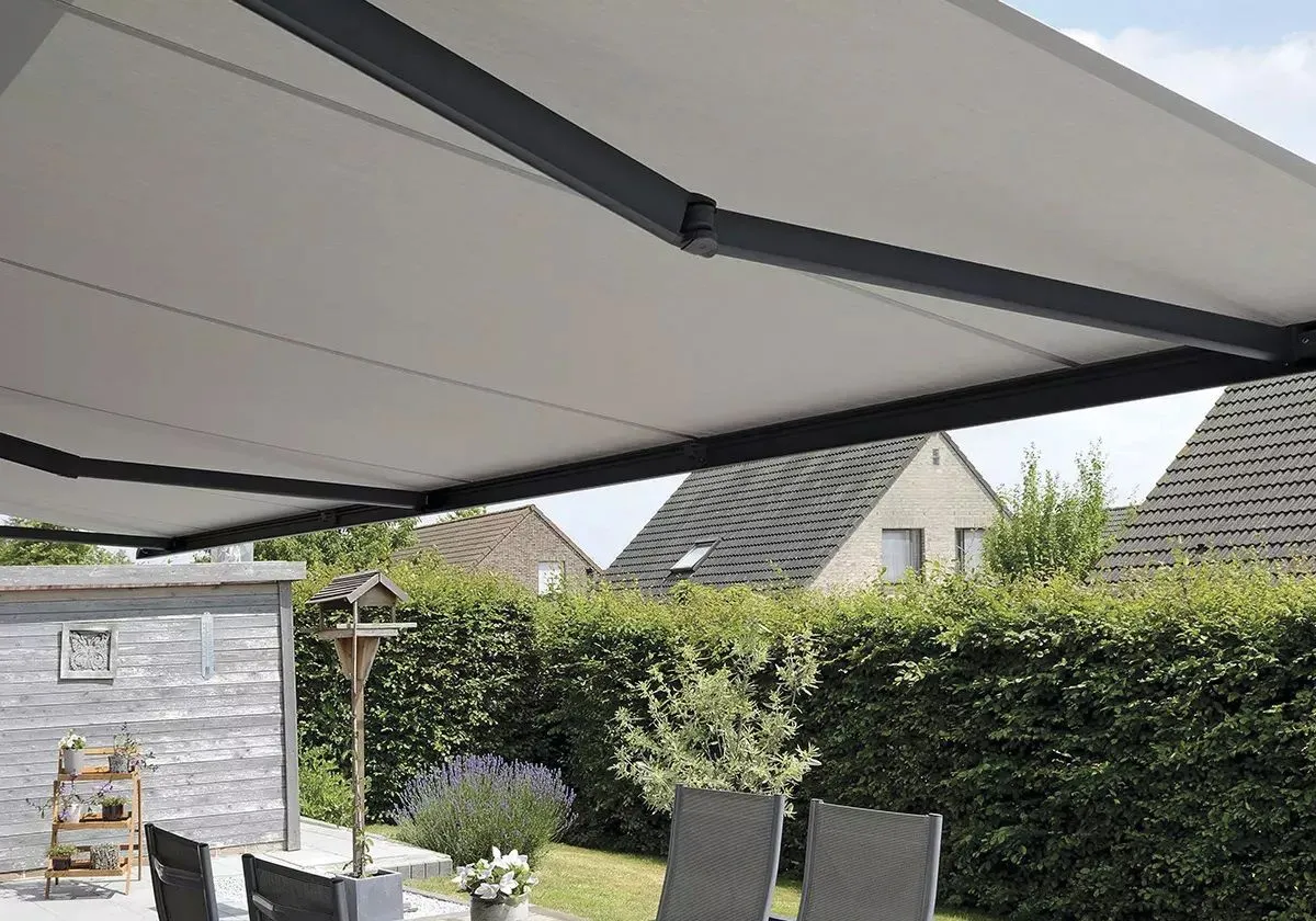 Store banne grand format déployé au-dessus d’une terrasse avec salon de jardin